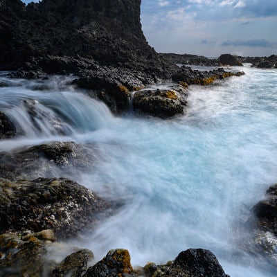 夕焼け空を背に打ち寄せる荒波と岩礁、白く泡立つ高波が激しく衝突する